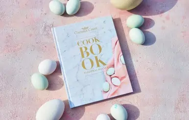 Cooking with Clarence cookbook on marble surface with pastel eggs.