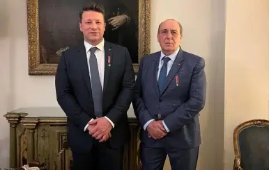 Two men in formal suits with medals, standing in an elegant room.