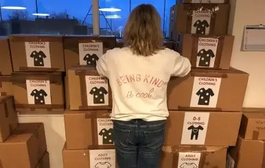 Child organizing boxes of donated children's clothing for charity.