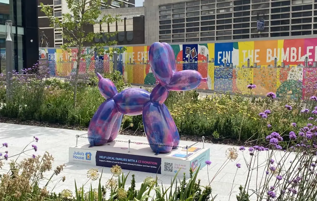 Shot of a Julia's House Swindog as part of the The Big Dog Art Trail in Swindon. The dog is purple and blue, and surrounded by wild flowers.