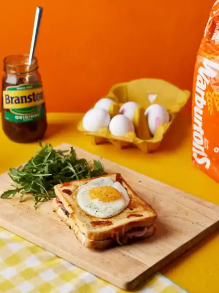 Breakfast toast with fried egg, greens, and Branston pickle on a wooden board.