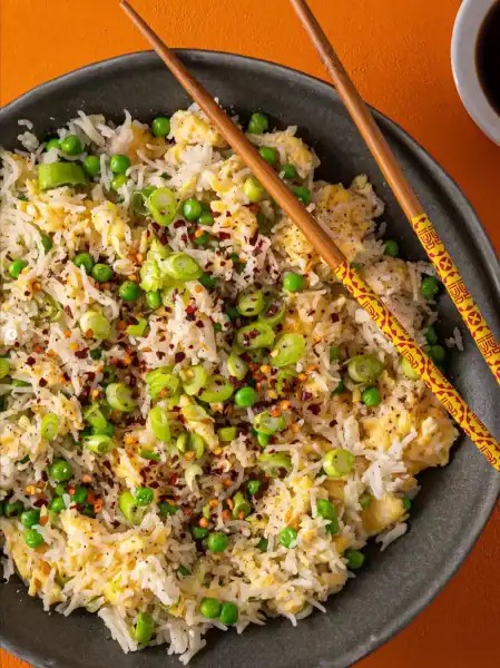 Asian fried rice with green peas, spring onions, and spices in a black bowl.