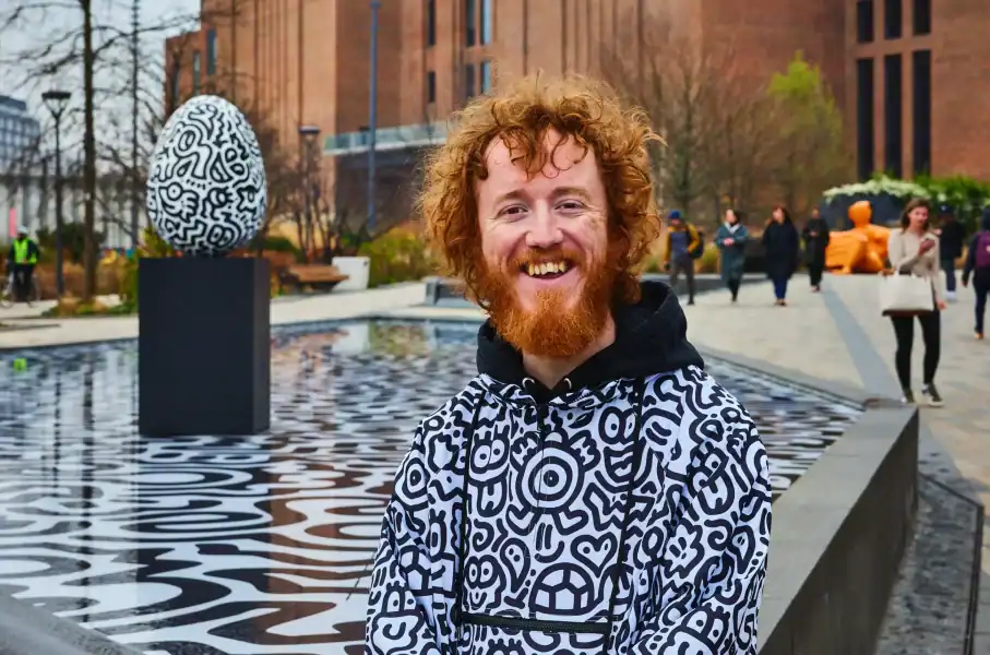 Smiling man at outdoor event with modern art sculpture in background.