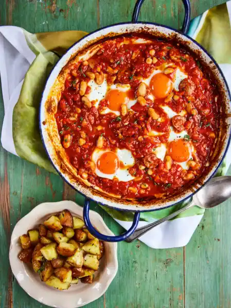 Bright image of shakshuka with eggs, tomato sauce, and vegetables in a skillet.