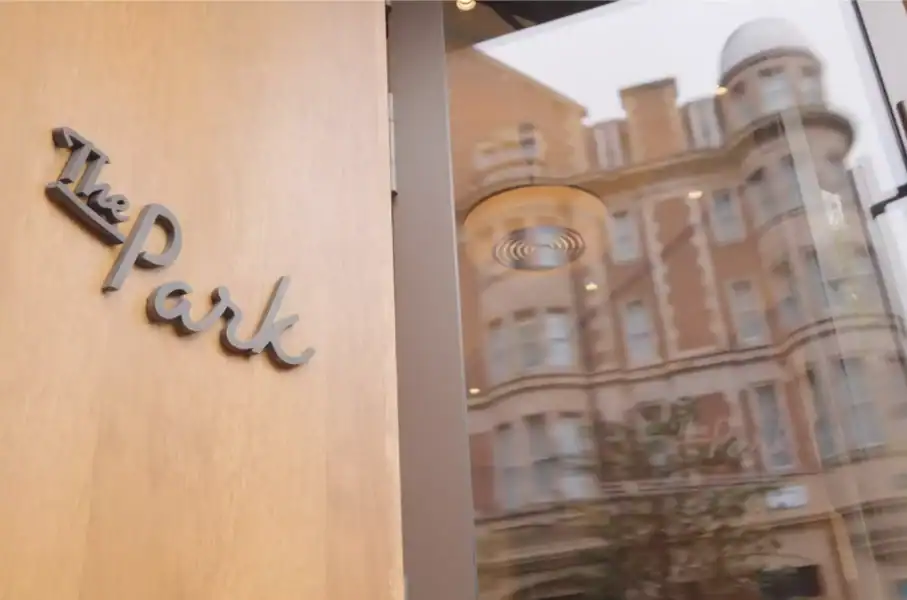 Close-up of The Park sign on a wooden wall with city buildings reflected in the glass.