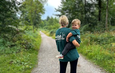 Woman holding a child on a forest trail, celebrating milestones outdoors.