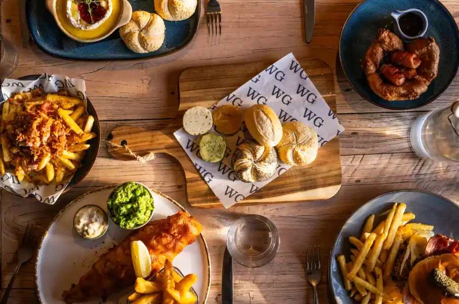 Assorted British pub dishes including fish and chips, fries, and fried chicken on a wooden table.